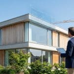 Un architecte utilisant une tablette numérique devant une maison moderne avec une interface holographique de normes.